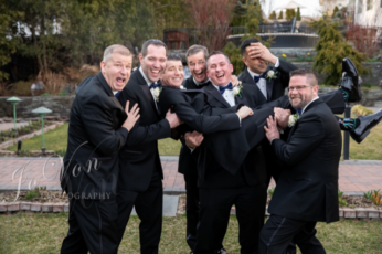 Groomsmen playfully lift friend at wedding.