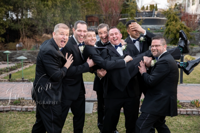 Groomsmen playfully lift friend at wedding.