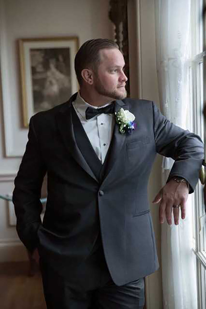 Groom in tuxedo looking out window.