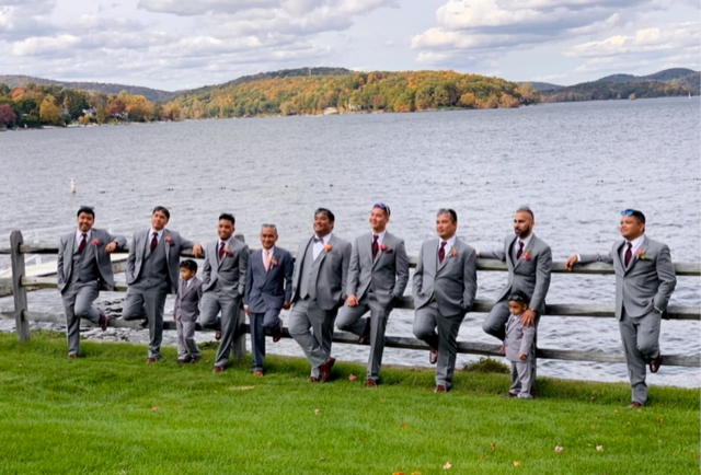 Groomsmen posing by lake in suits.