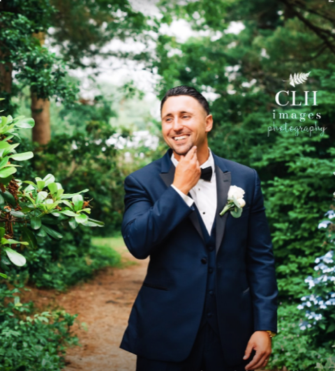 Smiling groom in navy tuxedo outdoors.