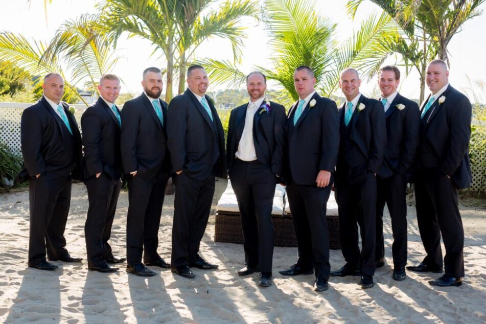 Groomsmen in black suits on beach.
