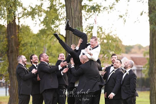 Groomsmen tossing groom in the air.