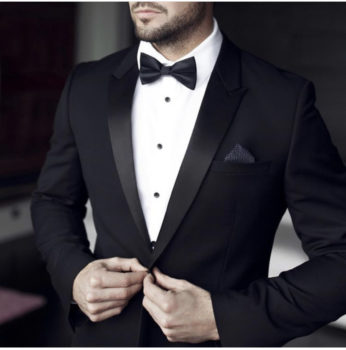 Man in black tuxedo adjusting jacket.