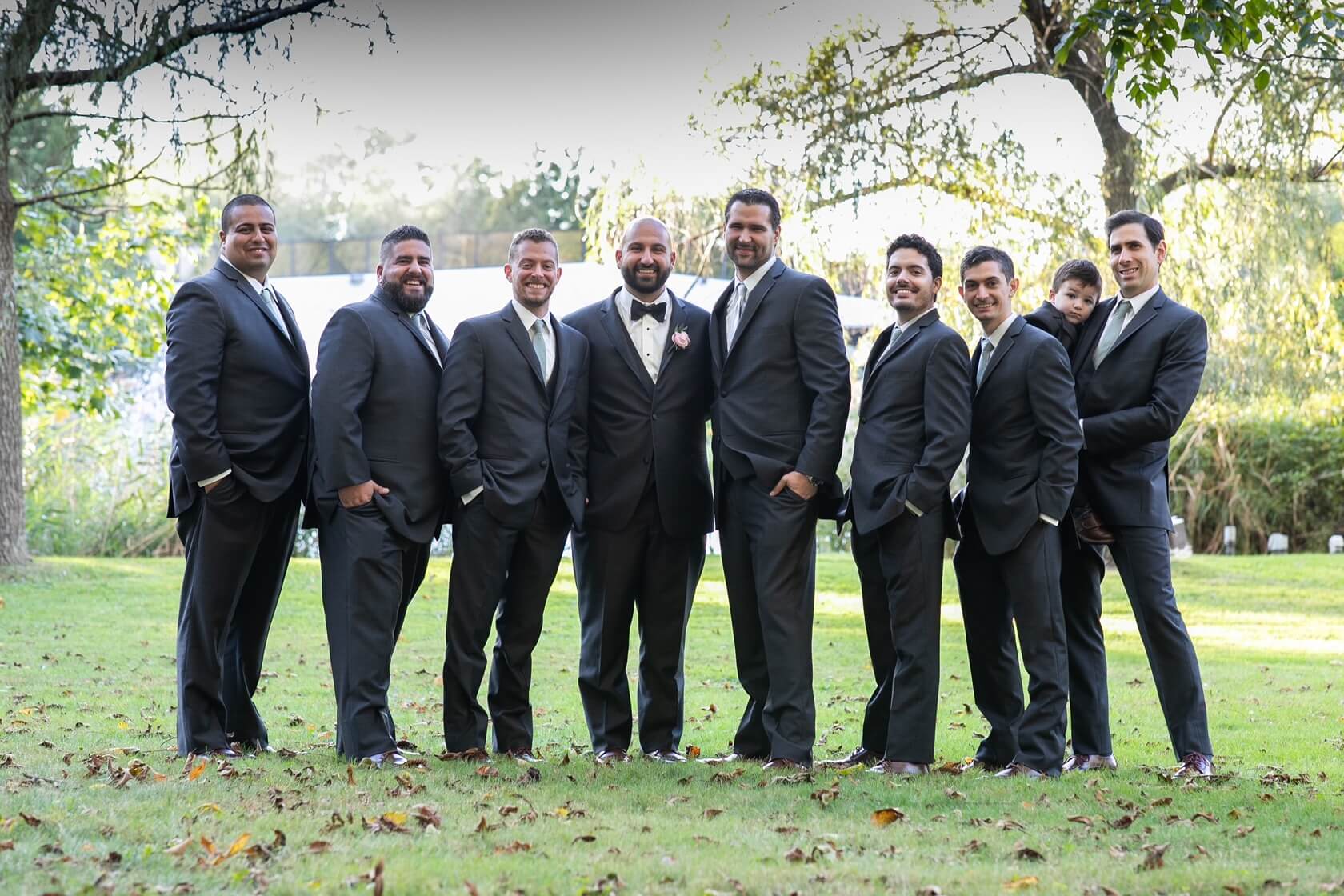 Groomsmen and child in suits outdoors.