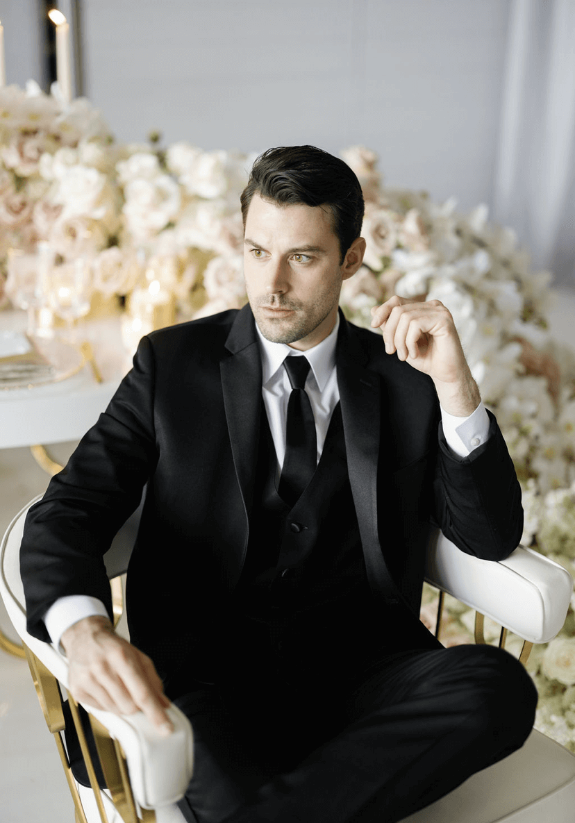 Man in black tuxedo sits thoughtfully.